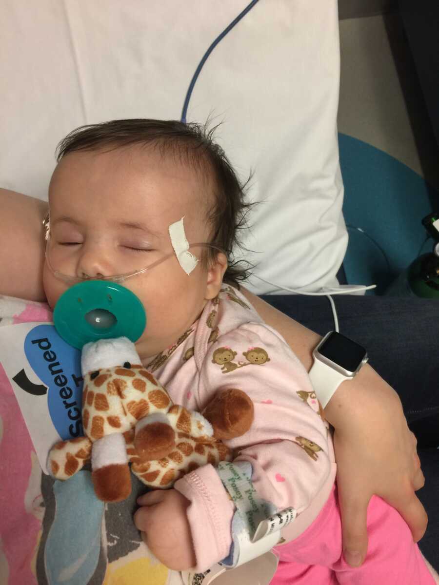 Baby with breathing tube sleeps with stuffed giraffe 