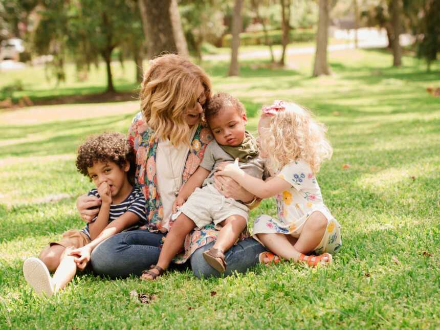 mother with 3 adopted children sitting in grass outside at park