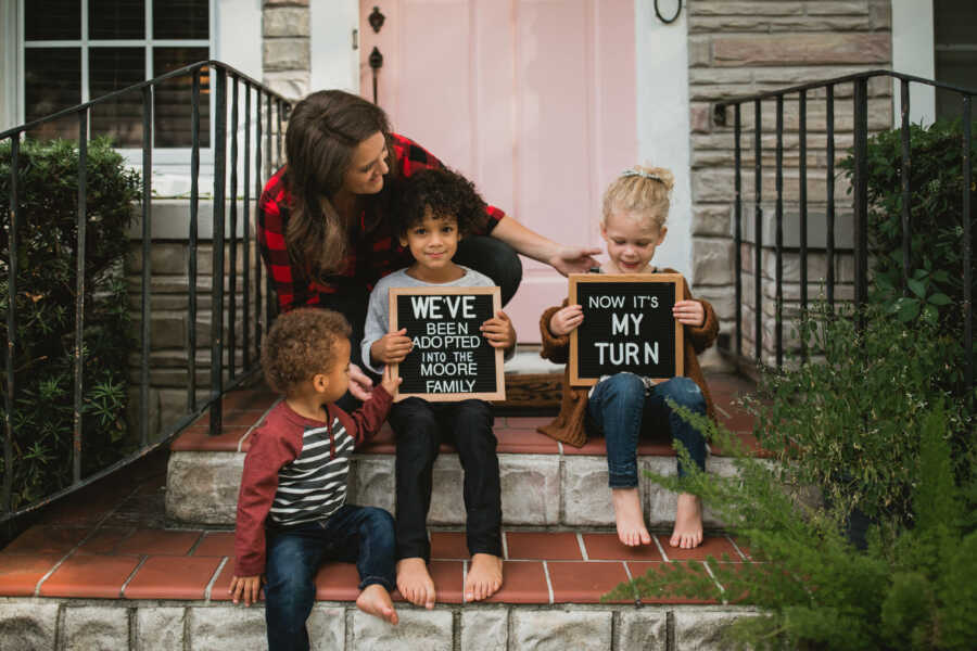mother with adopted kids holding black signs celebrating adoption on brick steps