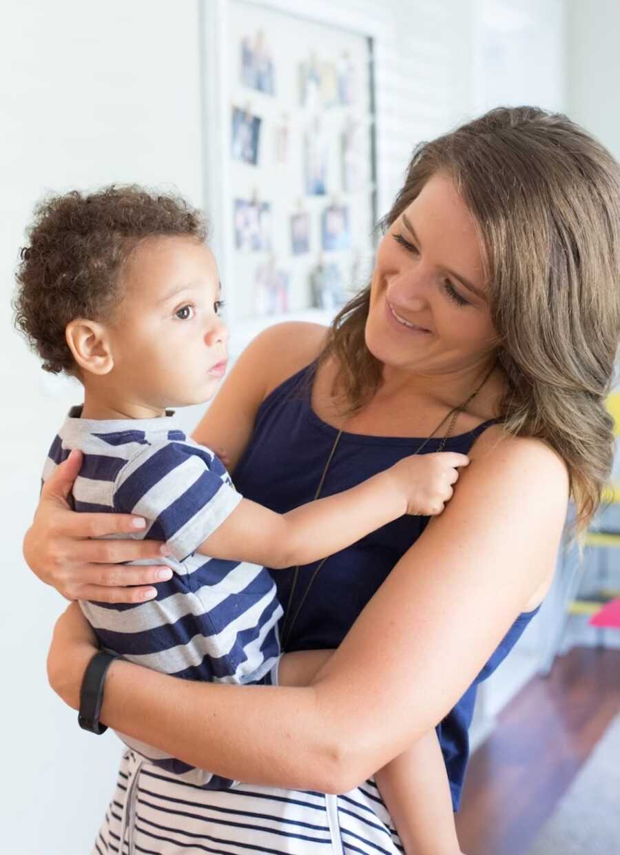 mother holding adopted baby boy that's wearing a white and blue striped shirt