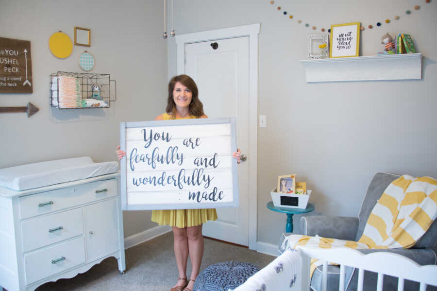 adoptive mother standing in baby nursery holding loving sign for foster babies